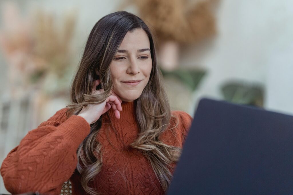 Woman in a sweater working on a laptop, exuding confidence and focus in a cozy, indoors setting.